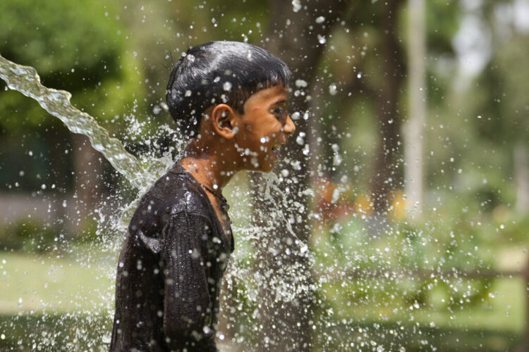 A boy cools himself under an irrigation water pipe  as northern Indian continues to reel under intense heat wave in Lucknow in the the Indian state of Uttar Pradesh, Wednesday, April 19, 2023. Temperatures in India have become dangerously hot because of climate change. Heat wave in many parts of India are impacting human lives, with nearly a dozen dead and crops impacted. Amid the soaring temperature, schools in some parts of India have closed while some have changed their timings too. (AP Photo/Rajesh Kumar Singh)